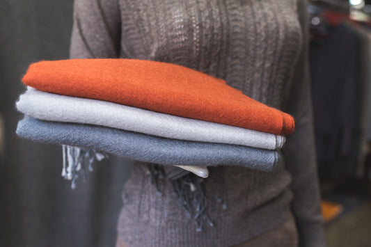   Save Download Preview close up of a person in a brown sweater with scarfs, close up of folded scarfs, orange white and grey cashmere clothes, a mannequin in a showroom, close up of colorful fabric