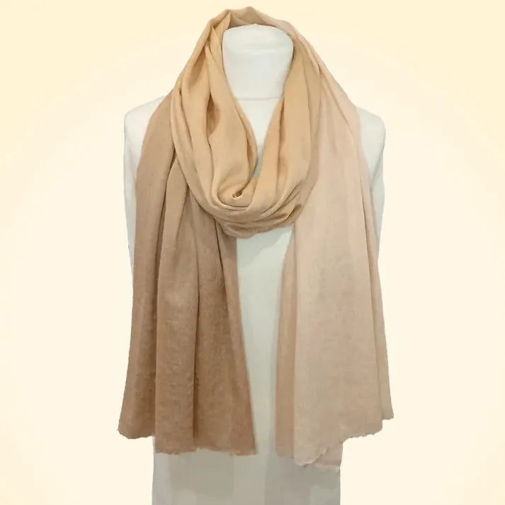 Model wearing large shaded pashmina cashmere stole wrapped around shoulders in a warm, rustic interior setting, highlighting its size and softness.