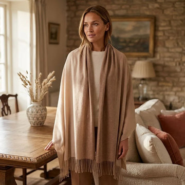 Model wearing large shaded pashmina cashmere stole wrapped around shoulders in a warm, rustic interior setting, highlighting its size and softness.